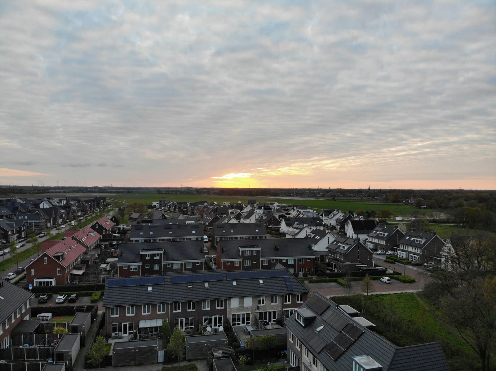 Daken van een woonwijk met tuinen en straten, schuin van boven gefotografeerd bij zonsondergang
